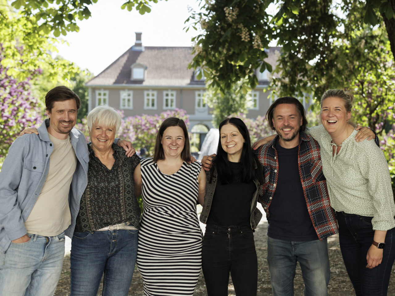 Michael, Anne Rita, Beate, Maren, Seth og Ane står oppstilt på rekke i en park. De smiler og holder rundt hverandre